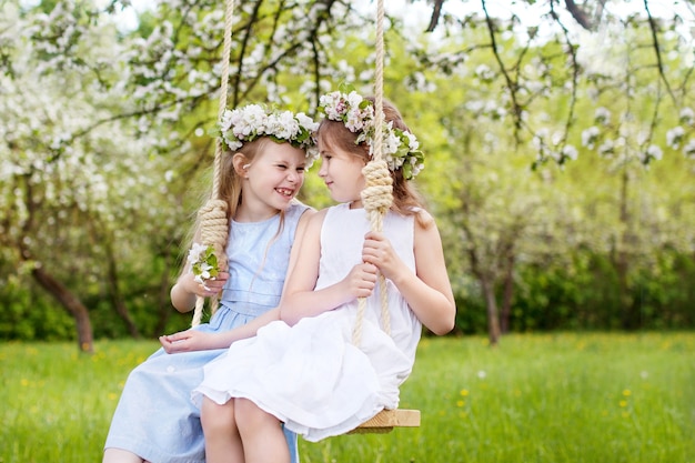 Due ragazze carine che si divertono su un'altalena nel vecchio giardino di melo in fiore. Giorno soleggiato. Attività all'aperto primaverili per bambini