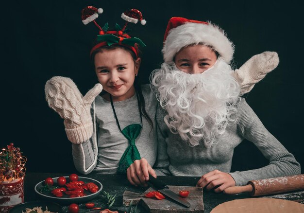 Due ragazze caucasiche in un cappello di Babbo Natale con una fascia e una fascia seduta felice a un tavolo