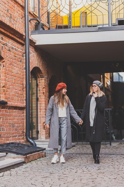 Due ragazze che camminano insieme per strada indossano abiti primaverili o autunnali e sono felici