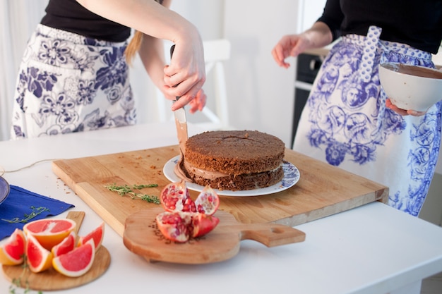 Due ragazze che fanno una torta sulla cucina. Mani delle donne, causando la crema al cioccolato