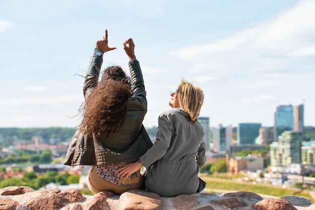 Due ragazze che mostrano il segno d'amore con le dita e si godono il concetto di panorama dello skyline della città