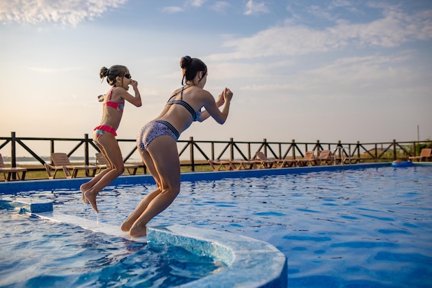 Due ragazze che si tuffano in piscina durante le vacanze estive al tramonto