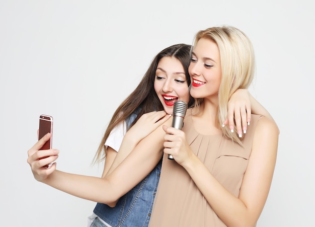 Due ragazze di bellezza con un microfono si fanno selfie con lo smartphone