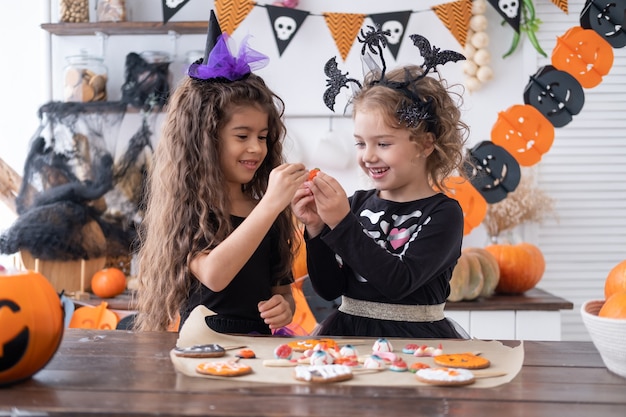 Due ragazze diverse in costume da strega, che si divertono a casa in cucina, festeggiano Halloween.