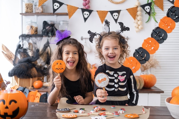 Due ragazze diverse in costume da strega, si divertono in cucina, mangiano biscotti, festeggiano Halloween.