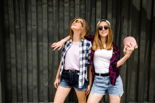 Due ragazze divertenti allegre che indossano camicie a scacchi in posa contro il muro di strada in strada.