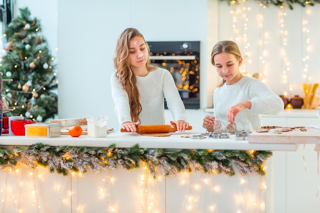 Due ragazze felici che cucinano facendo il pan di zenzero, tagliando i biscotti di pasta di pan di zenzero, divertendosi.