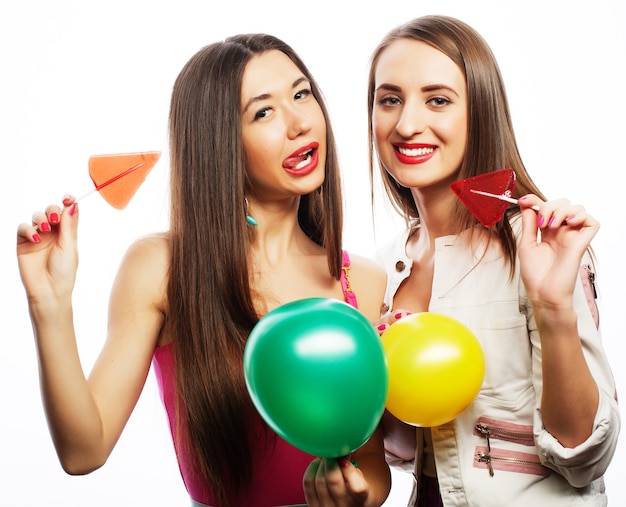 Due ragazze felici che sorridono e tengono in mano palloncini colorati e caramelle