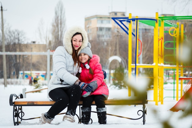 Due ragazze felici, madre e figlia seduti su una panchina in un parco giochi nel parco cittadino.