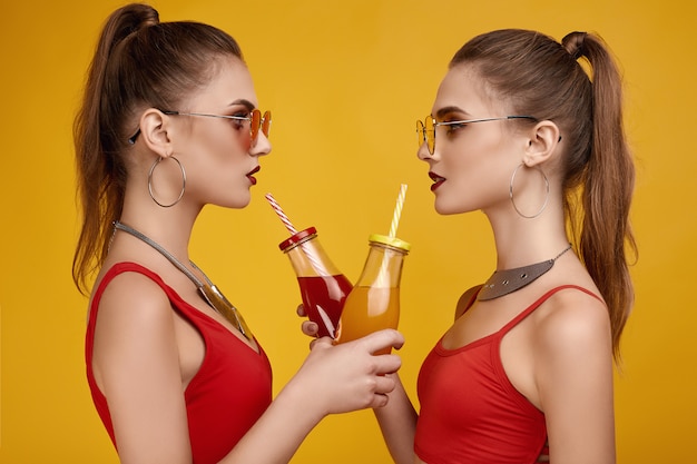 Due ragazze gemelle di hipster glamour elegante in top rosso moda con cocktail drink