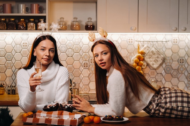 Due ragazze in un accogliente ambiente domestico con champagne in mano a Natale. Le ragazze sorridenti bevono champagne in una serata festiva