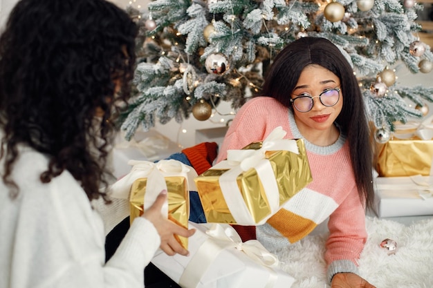 Due ragazze indiane con gli occhiali che si siedono vicino all'albero di Natale