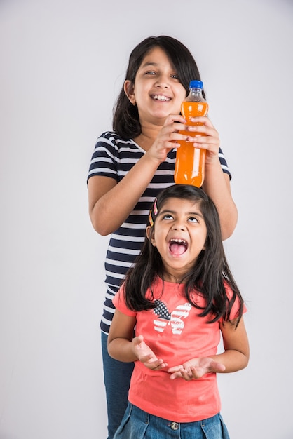 Due ragazze indiane con una bottiglia di bevanda fredda, due ragazze asiatiche in posa con una bevanda fredda in una bottiglia di animali domestici, 2 ragazze e una bevanda fredda, ragazze indiane carine che giocano con succo di mango o bottiglia di succo d'arancia