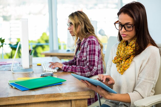 Due ragazze lavorano in ufficio su computer e tablet