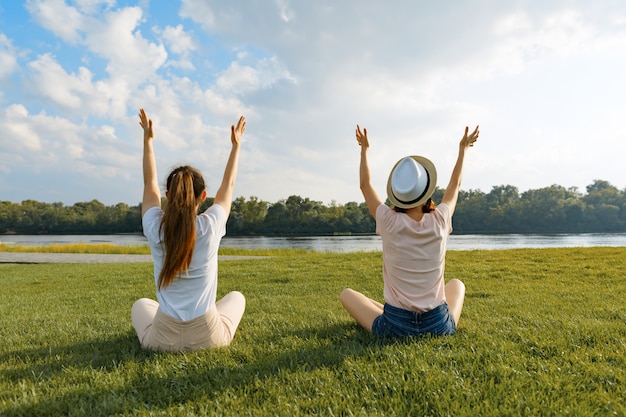 Due ragazze meditano nel parco vicino al fiume, vista posteriore