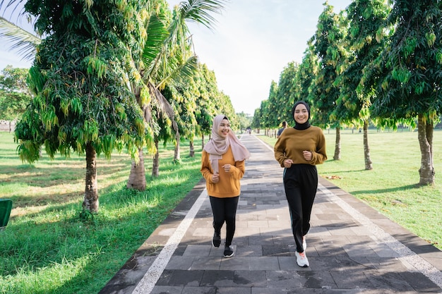 Due ragazze musulmane felici in velo fanno sport all'aria aperta mentre fanno jogging insieme nel parco