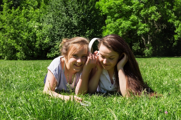 Due ragazze più giovani e più grandi ascoltano musica al telefono Trascorrendo del tempo con un amico nel parco