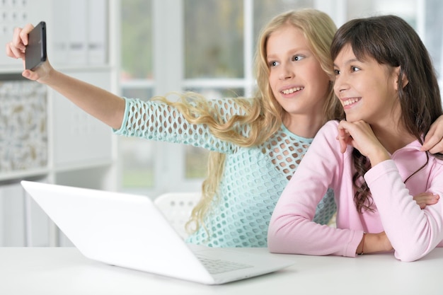 due ragazze sedute davanti al laptop e che si fanno selfie con il telefono