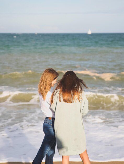 Due ragazze sono in piedi sulla spiaggia in una giornata di sole Pantaloni a vita bassa alla moda vicino alle onde del mare Donne che parlano Concetto di viaggio per le vacanze Barcellona Spagna