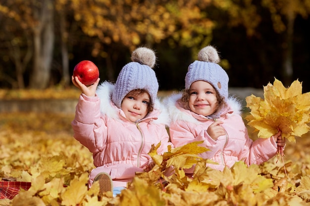 Due ragazze, sorelle in abiti e cappelli sono seduti su foglie gialle in autunno parco sulla natura.