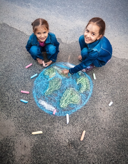 Due ragazze sorridenti che disegnano la Terra con i gessetti per strada