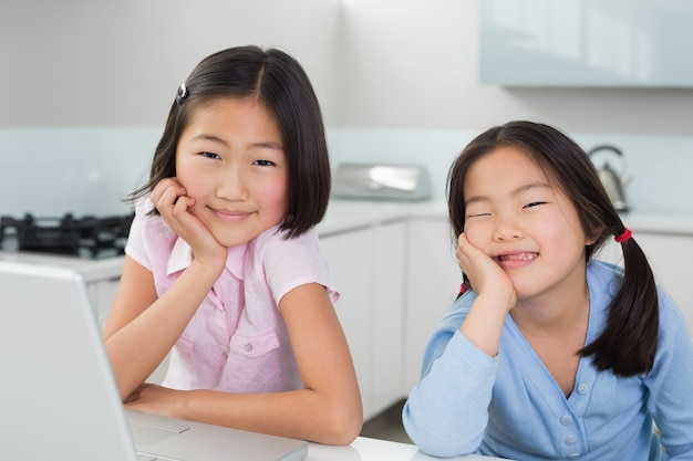 Due ragazze sorridenti con il computer portatile in cucina