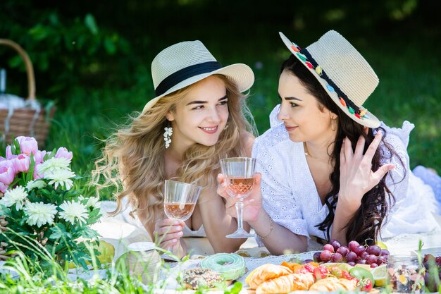 Due ragazze stanno riposando nel parco sedute su una coperta da picnic con frutta e vino