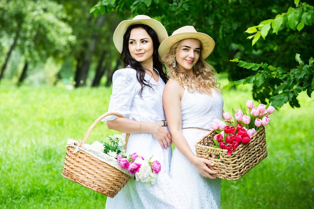 Due ragazze stanno riposando nel parco sedute su una coperta da picnic con frutta e vino