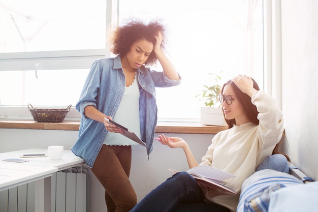 Due ragazze stanno tenendo le mani vicino alle teste. Stanno studiando materie difficili. Sono frustrati e infelici.