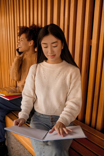 Due ragazze su una panchina, una che studia, un'altra che parla al telefono