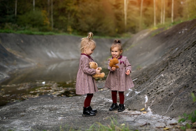 Due ragazze tra i grigi pendii rocciosi di un bosco da favola tengono in mano degli orsacchiotti