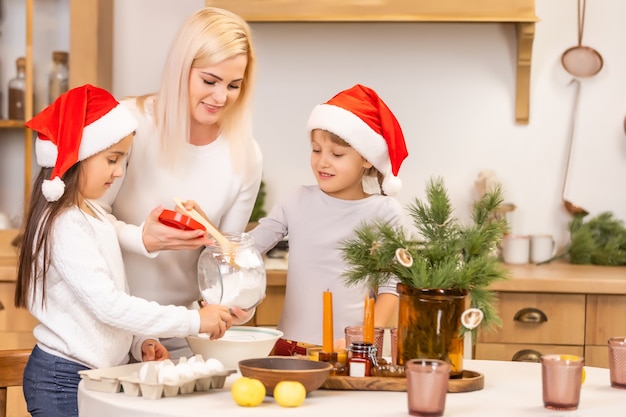 Due ragazze vestite con cappelli rossi stanno preparando biscotti, pan di zenzero per le vacanze di Capodanno, Natale. Ritaglia i biscotti.