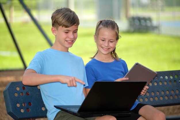Due ragazzi adolescenti che tengono un computer portatile e una bella ragazza con tablet digitale che studiano insieme all'aperto seduti su una panchina Istruzione durante il concetto di quarantena