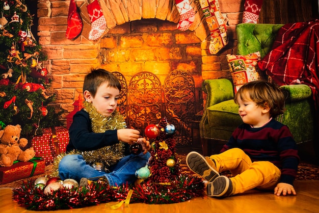 Due ragazzi biondi che giocano con le decorazioni di Natale davanti al caminetto. buon Natale.