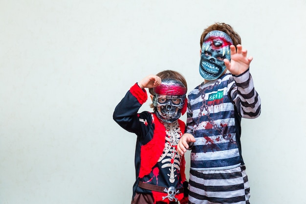 Due ragazzi che indossano un costume spaventoso con maschere su sfondo chiaro, copia spazio. Bambini che si preparano alla festa di Halloween in ottobre.