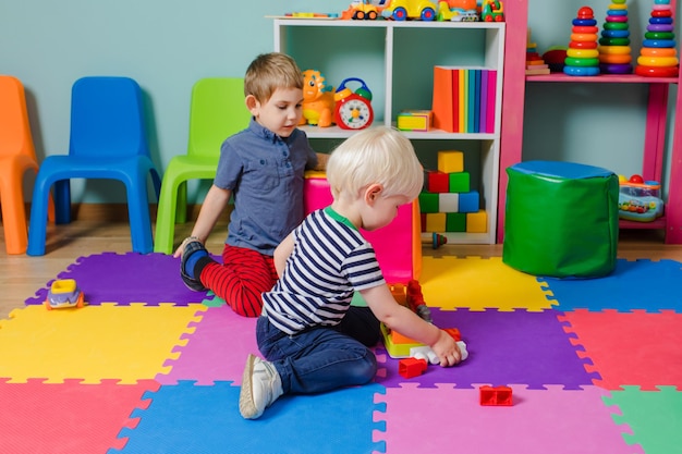 Due ragazzi nella scuola materna che giocano con i giocattoli da costruzione Sullo sfondo del ragazzo c'è un altro bambino che gioca con un giocattolo