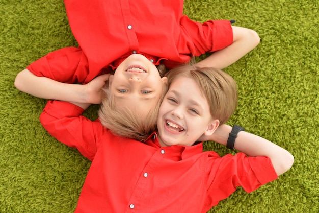 Due ragazzi sorridenti in camicie rosse sdraiati sul pavimento con un tappeto verde