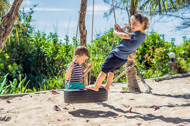 Due ragazzini biondi si divertono sull'altalena sulla costa sabbiosa tropicale