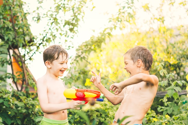 Due ragazzini che giocano con pistole ad acqua in una calda giornata estiva bambini carini che si divertono con l'acqua sul