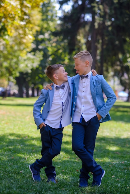 Due ragazzini, i fratelli sono vestiti con un abito. I bambini sono in piedi nel parco e si abbracciano. I ragazzi si mostrano l'un l'altro la lingua.