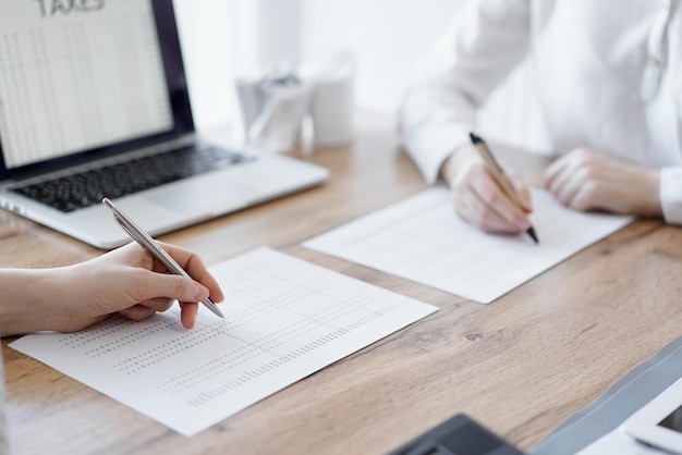 Due ragionieri che utilizzano un computer portatile e una calcolatrice mentre contano le tasse alla scrivania di legno in ufficio. Lavoro di squadra nel controllo aziendale e nella finanza