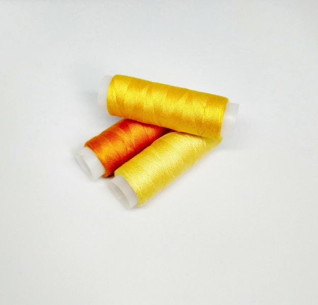 Due rocchetti di filo giallo con un filo rosso su sfondo bianco.