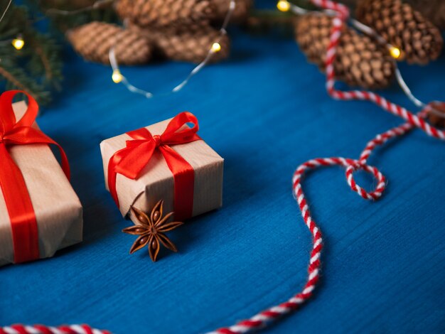 Due scatole regalo su un tavolo di legno blu, rami di un albero di Natale con coni e palline rosse