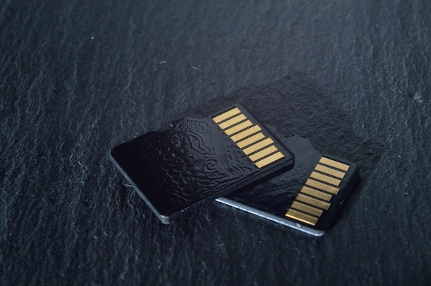 Due schede micro sd si trovano una sopra l'altra su uno sfondo strutturato scuro, con contatti dorati nella parte superiore. avvicinamento.