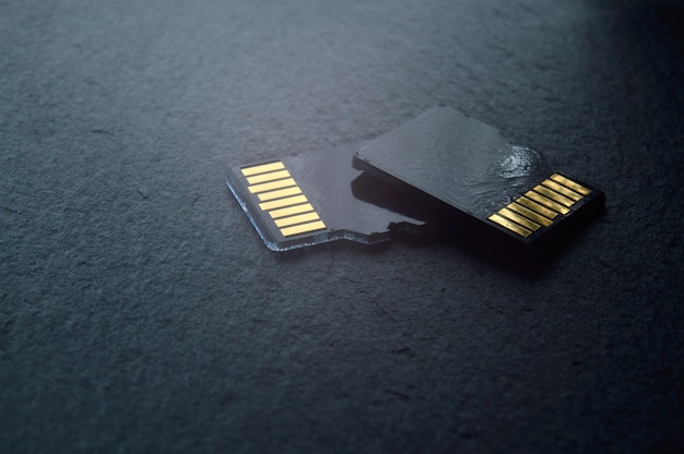 Due schede micro sd si trovano una sopra l'altra su uno sfondo strutturato scuro, con contatti dorati nella parte superiore. avvicinamento.