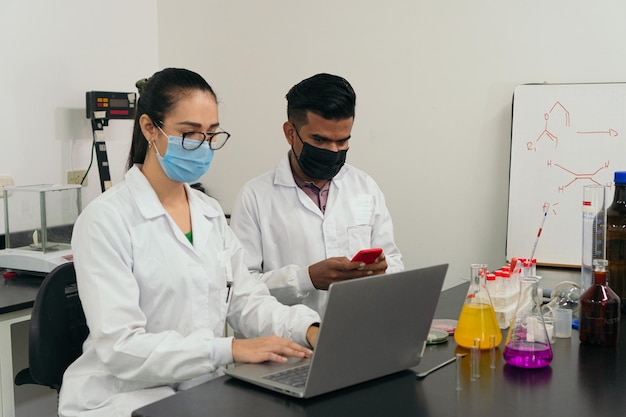 Due scienziati che lavorano su un laptop in laboratorio Indossando maschere protettive come nuova normalità durante la pandemia di COVID19