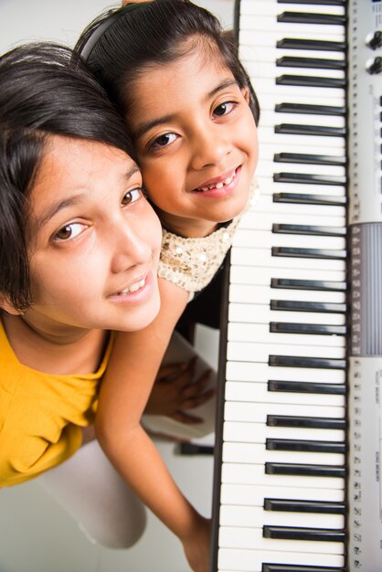 Due simpatiche ragazze indiane o asiatiche che suonano il pianoforte o la tastiera, uno strumento musicale, su sfondo bianco