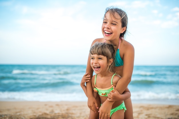 Due simpatiche sorelle bambine positive hanno alzato le mani mentre nuotavano in mare durante le vacanze in una calda giornata estiva. Concetto di bambini sani e gioiosi