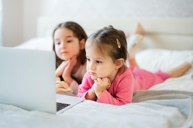 Due simpatiche sorelline indossano un pigiama che sembra un cartone animato al computer portatile al mattino a casa