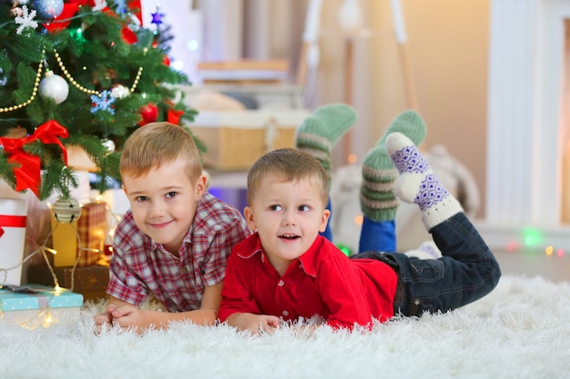 Due simpatici fratellini giacciono su un tappeto sullo sfondo dell'albero di Natale